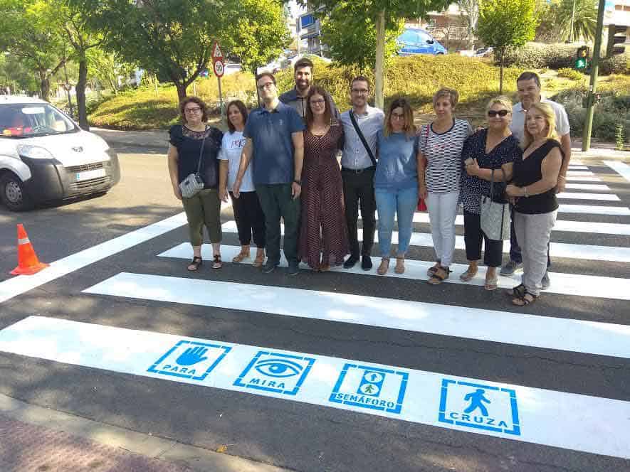 un grupo de personas mirando a la cámara sobre un paso peatonal que en su primera línea tiene cuatro símbolos que indican: "para", "mira", "semáforo".