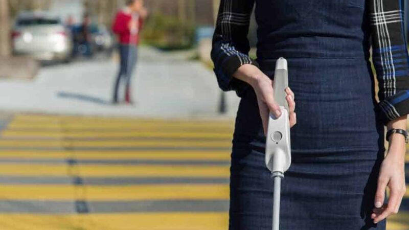 Una mujer cruzando un paso peatonal utilizando un bastón que incluye botones con diferentes funciones.