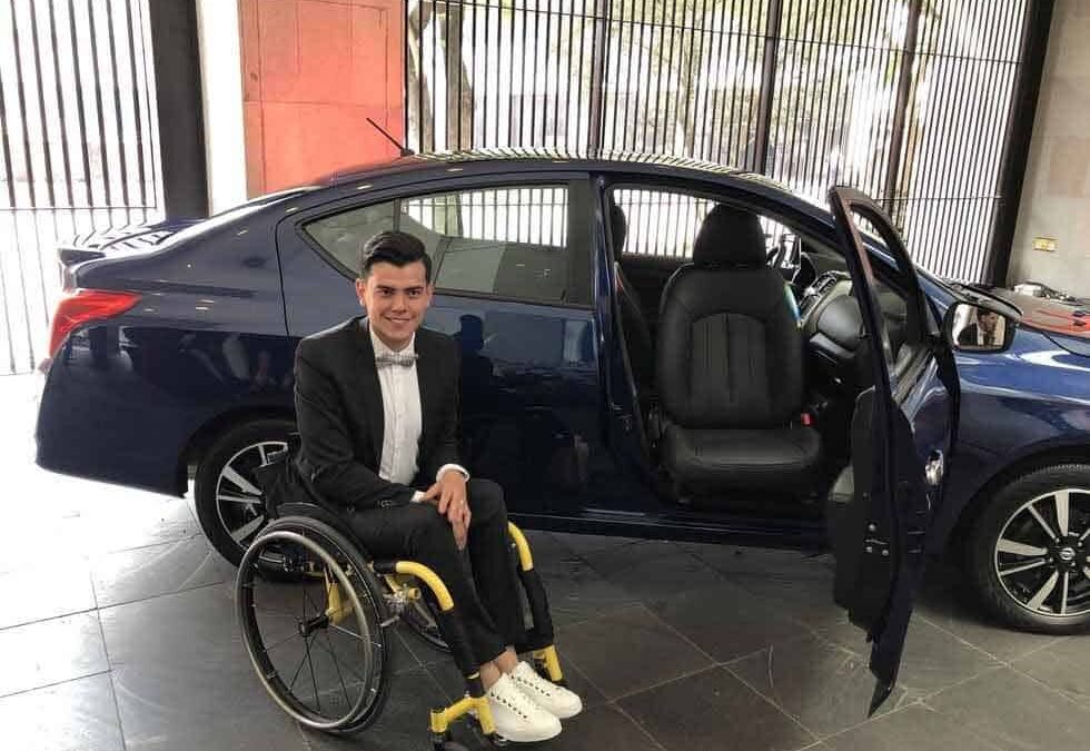 Un joven en silla de rudas posa para la foto al lado del nuevo auto adaptado
