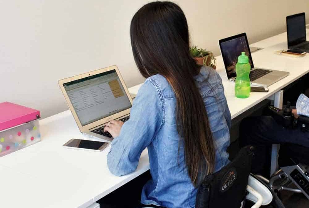 Una mujer en silla de ruedas trabajando en su escritorio con su computador.