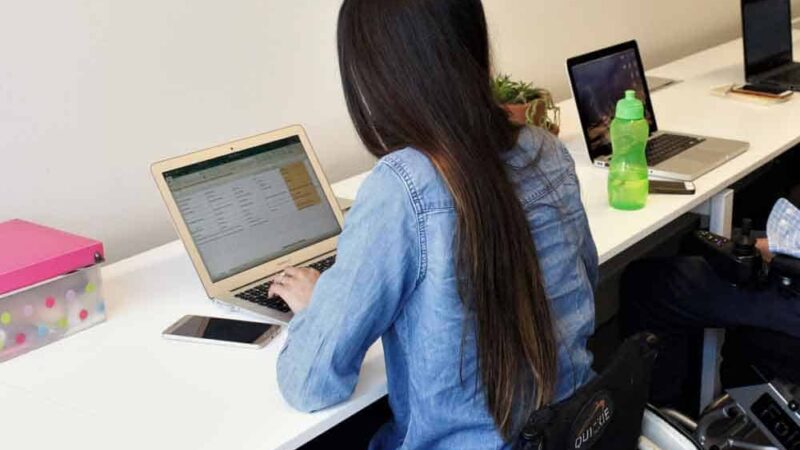 Una mujer en silla de ruedas trabajando en su escritorio con su computador.