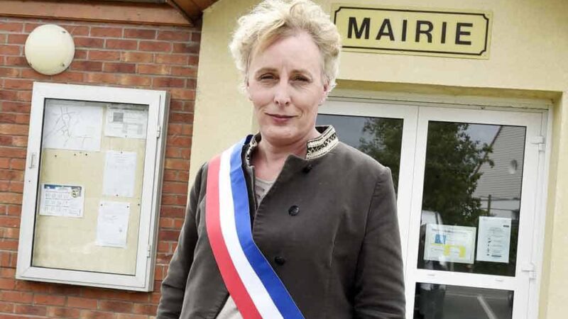 Aparece una mujer trans con una banda presidencial con los colores de Francia. Está afuera de la municipalidad donde trabaja.