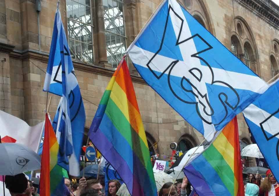 Foto de una manifestación LGBTI en Escocia donde están mezcladas banderas del arcoiris con banderas esocesas.