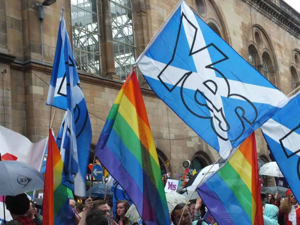 Foto de una manifestación LGBTI en Escocia donde están mezcladas banderas del arcoiris con banderas esocesas.