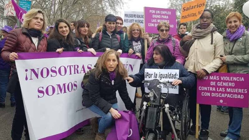 foto de un grupo de mujeres en situación de discapacidad en la calle durante una marcha. La mayoría viste de morado o tiene algún accesorio de ese color. Tienen diferentes carteles y uno de ellos dice "No más violencia de género contra las mujeres con discapacidad".