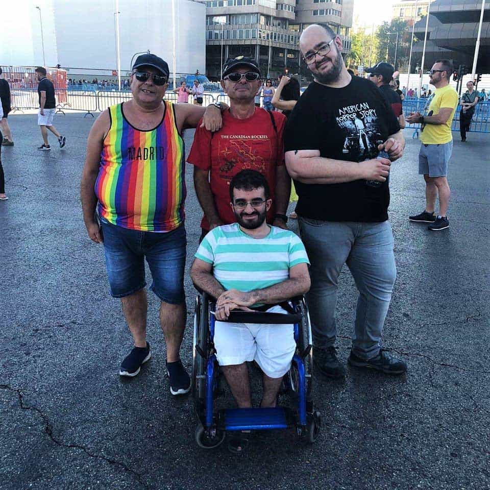 Foto donde aparecen 4 personas posando para la foto durante una marcha del Orgullo LGBTI en España. Están abrazados y uno de ellos está en silla de ruedas.