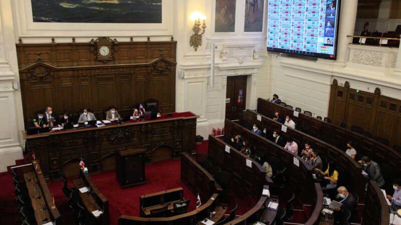 Foto de un salón grande donde se realiza el pleno de la convención constitucional y se ven varios asientos y arriba una pantalla con los resultados de la votación.