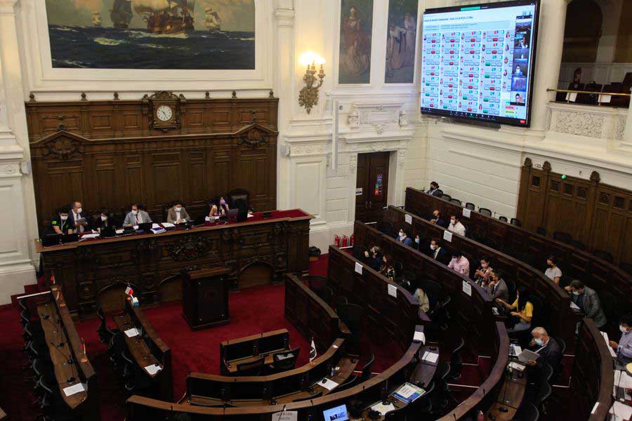 Foto de un salón grande donde se realiza el pleno de la convención constitucional y se ven varios asientos y arriba una pantalla con los resultados de la votación.