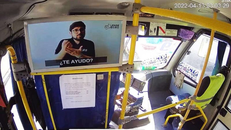 Foto dentro de una micro y en la parte de adelante de la micro hay una pantalla que muestra a una persona enseñando lengua de señas.