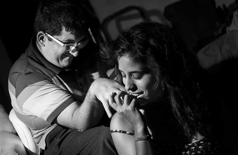 Foto de una pareja, donde uno de ellos tiene discapacidad intelectual y su pareja le besa la mano mientras el sonríe.
