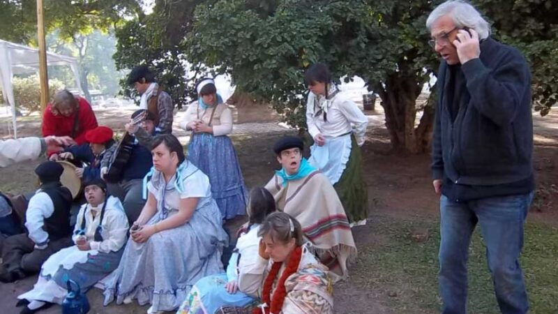 Foto donde aparecen unas 10 personas con algún tipo de discapacidad sentadas en una plaza durante una grabación y con vestimentas antiguas.