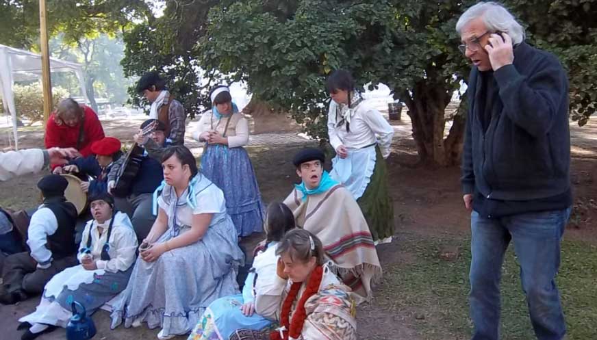 Foto donde aparecen unas 10 personas con algún tipo de discapacidad sentadas en una plaza durante una grabación y con vestimentas antiguas.