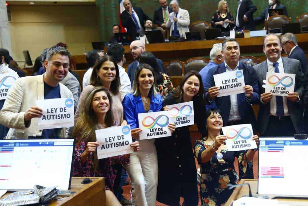 Foto dentro de la cámara de diputados donde aparece un grupo de diputados y diputadas sosteniendo carteles que dicen ley de autismo