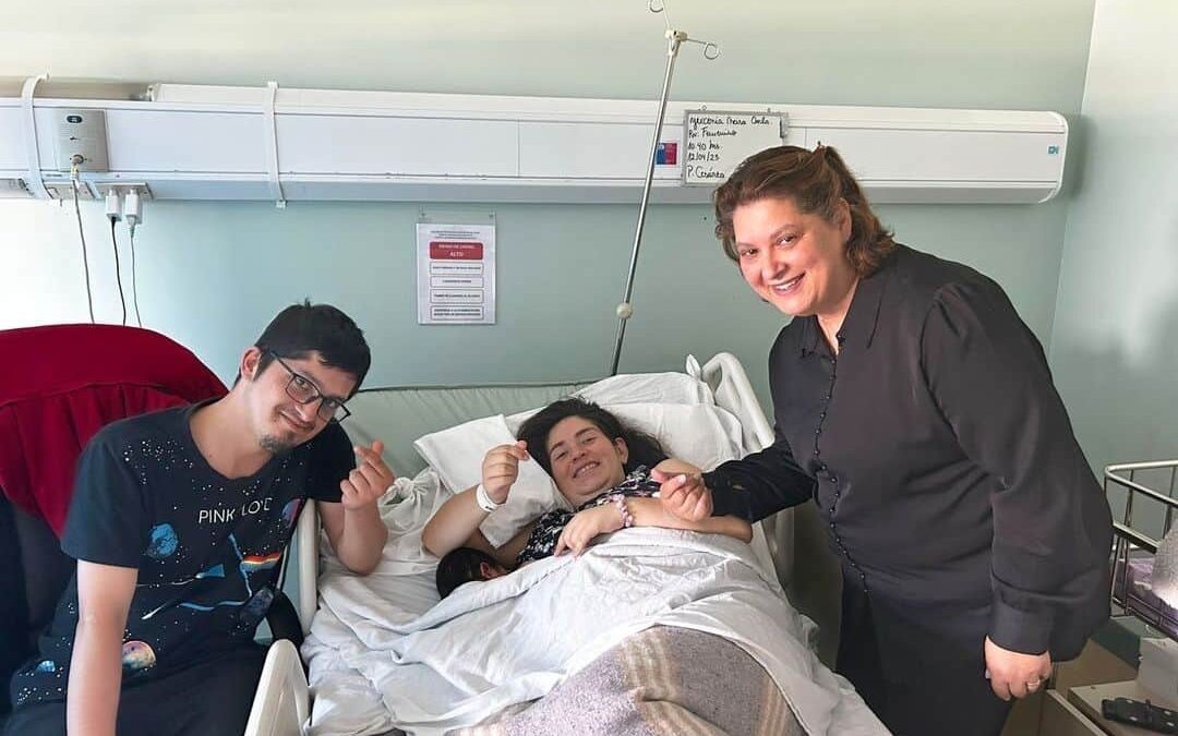 Foto en la pieza de un hospital donde aparece una mujer que acaba de parir acostada en su cama, sonriendo y acompañada de su pareja y al otro lado aparece la intérprete que la acompañó durante el proceso.