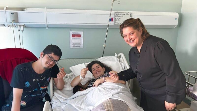 Foto en la pieza de un hospital donde aparece una mujer que acaba de parir acostada en su cama, sonriendo y acompañada de su pareja y al otro lado aparece la intérprete que la acompañó durante el proceso.