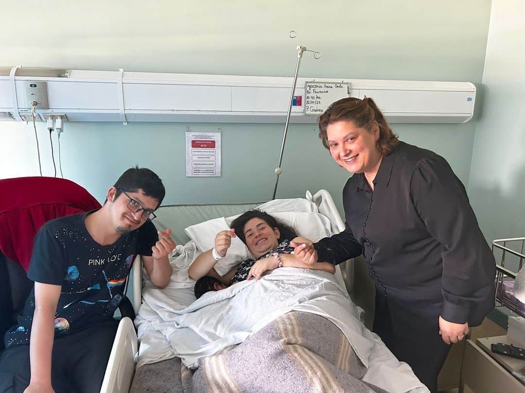 Foto en la pieza de un hospital donde aparece una mujer que acaba de parir acostada en su cama, sonriendo y acompañada de su pareja y al otro lado aparece la intérprete que la acompañó durante el proceso.