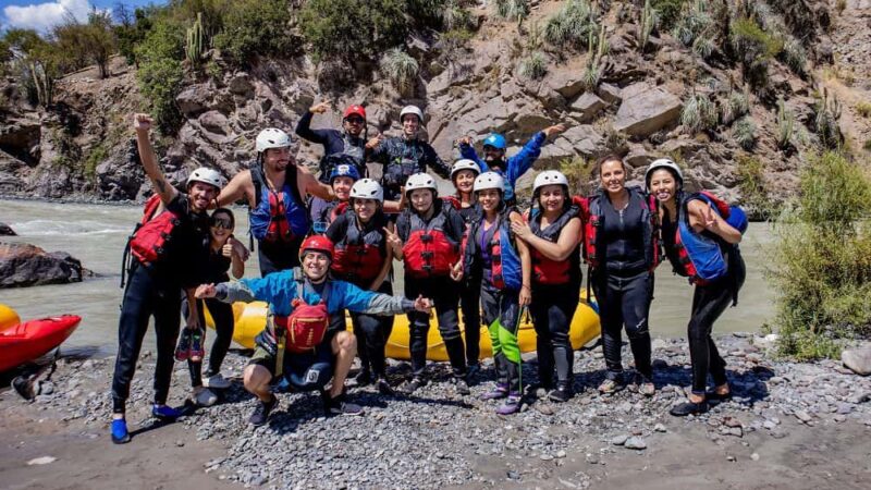 Foto de un grupo de personas sordas junto a interprete de lengua de señas y guía turístico, al borde de un rio, con el cerro de fondo, y con trajes de agua sonriendo a la cámara.