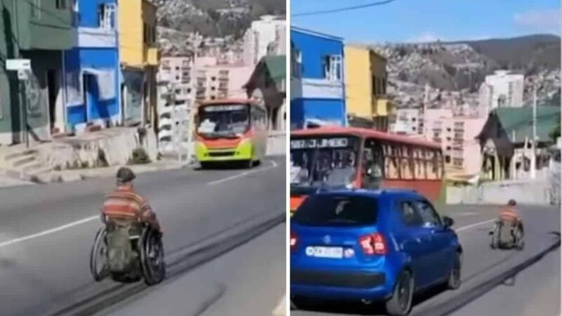 Pantallazo de un video donde aparece una persona en silla de ruedas bajando por una calle en un cerro de valparaíso, y de frente hay una micro y atrás de él viene un auto que lo intenta adelantar.