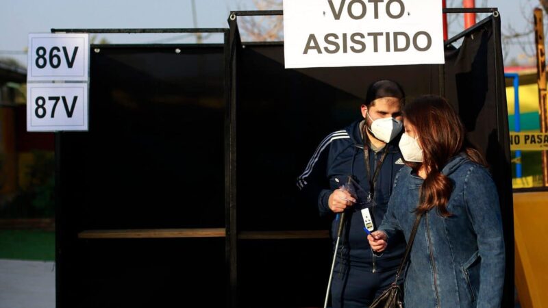 Foto de una persona ciega siendo acompañada por otra persona en la urna de votación.