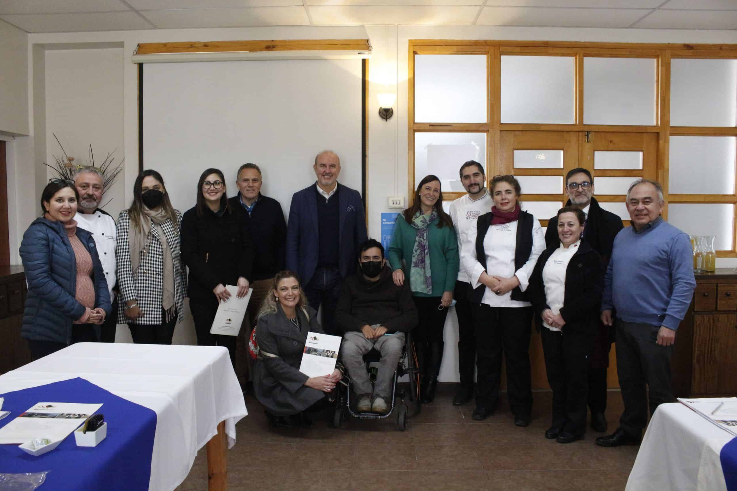 Foto en un salón del colegio achura de las condes donde hay un grupo de 15 personas posando para la foto después de una reunión de trabajo. Una de ellas está en silla de ruedas.