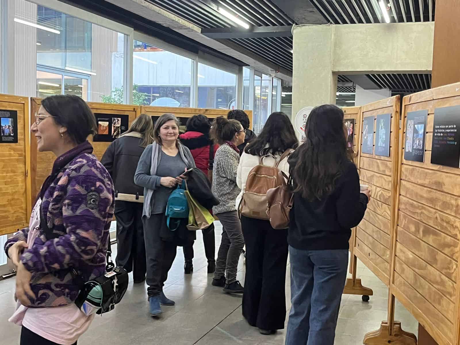 Dentro de un salón, hay un grupo de personas observando detenidamente unas fotos que se exponen en las paredes del lugar.