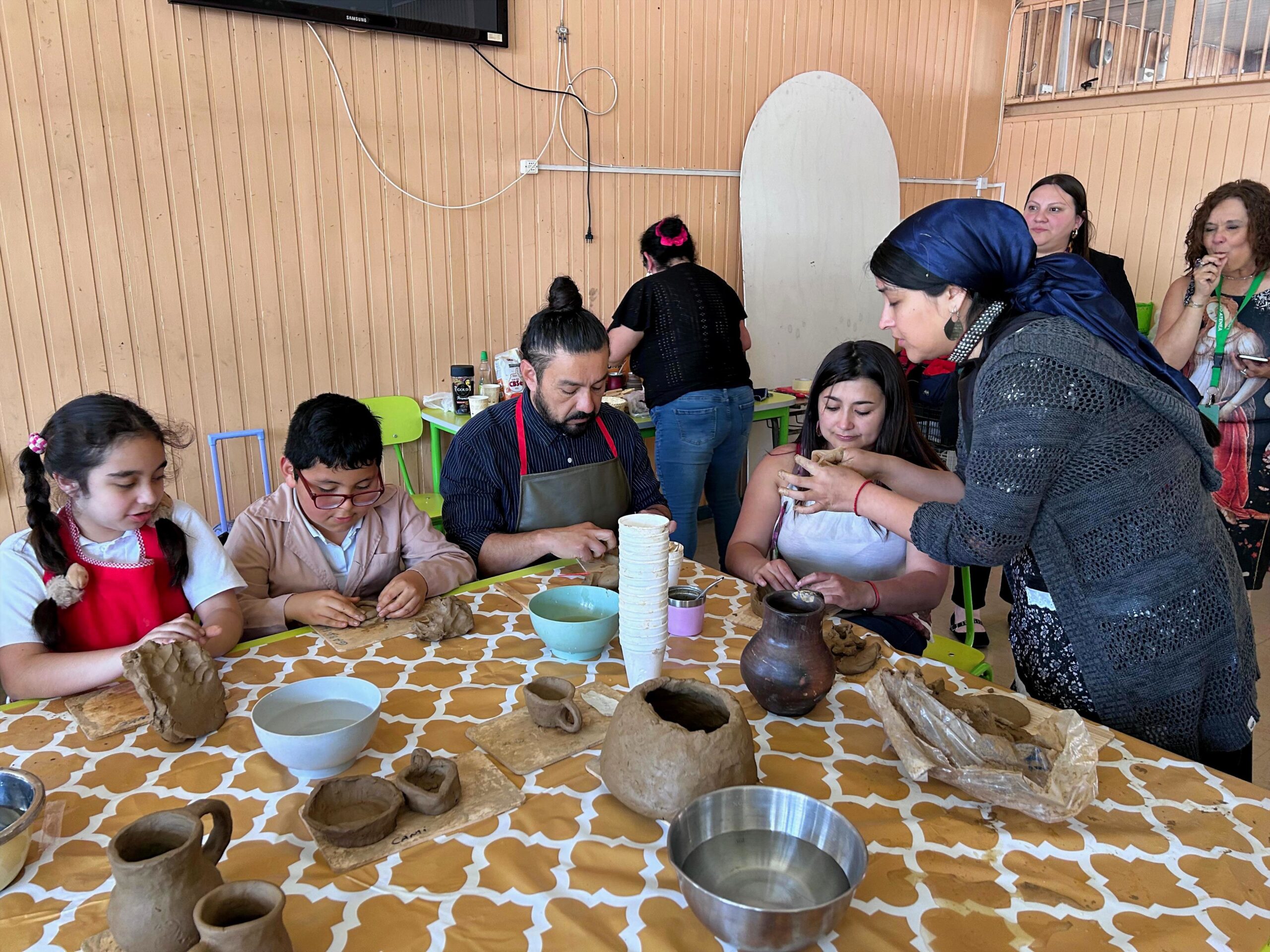 Niñas y niños mapuche sentados en torno a una mesa y trabajando con greda