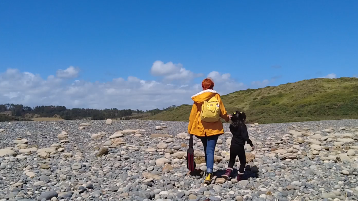 Niña de la mano de su mamá caminando por la playa, de espaldas ambas