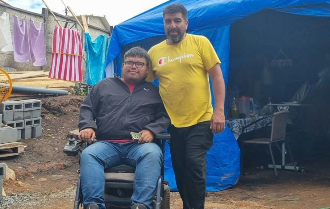 Hombre de pie abrazando a otro hombre en silla de ruedas