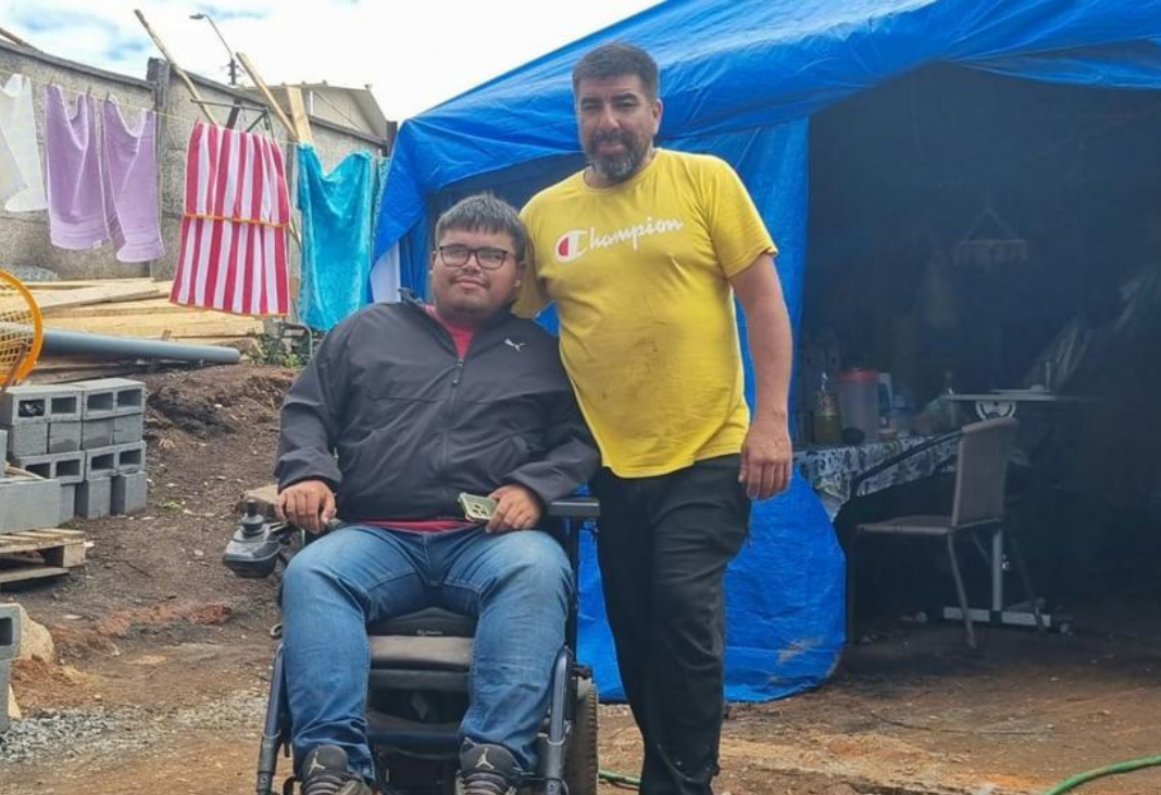 Hombre de pie abrazando a otro hombre en silla de ruedas