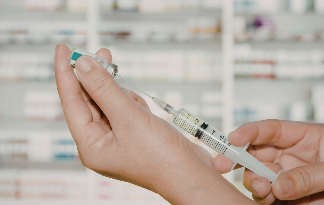 Mano llenado una jeringa con una ampolla y de fondo medicamentos