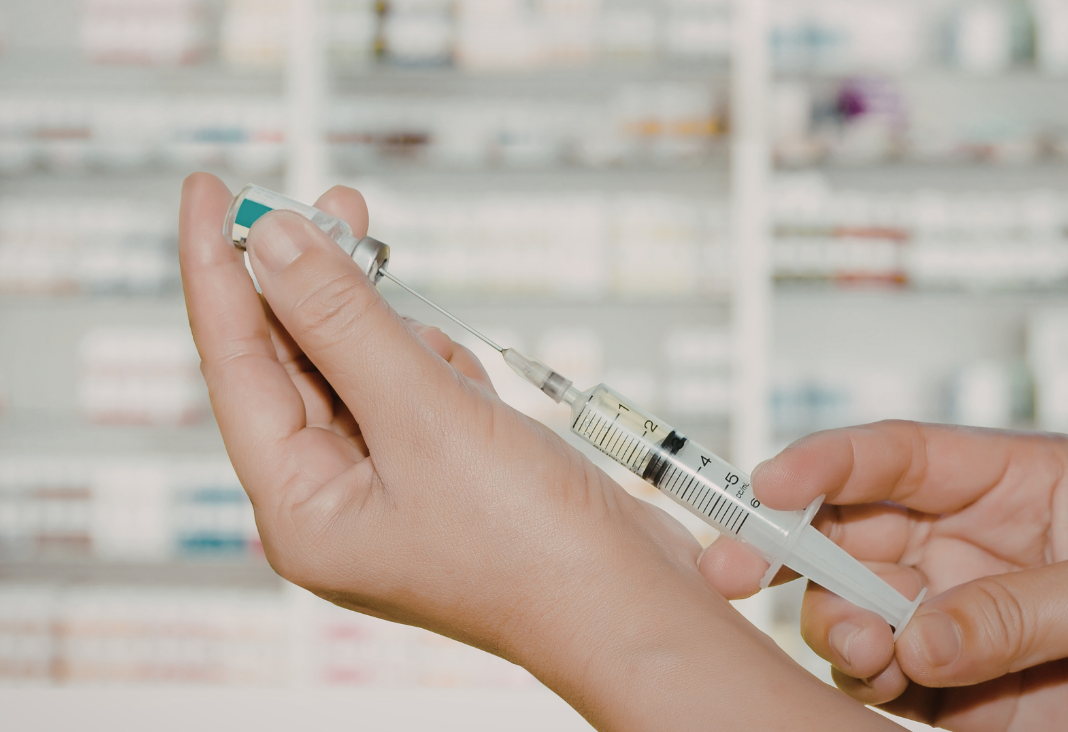 Mano llenado una jeringa con una ampolla y de fondo medicamentos