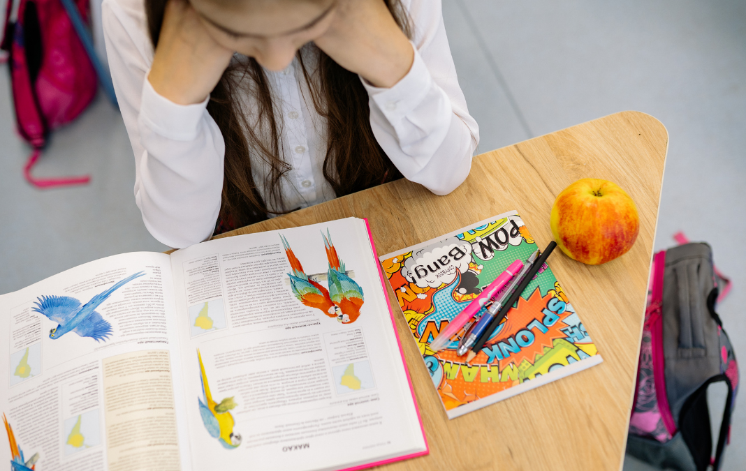 Niña mirando una mesa donde hay un libro, lápices, una manzana y lápices