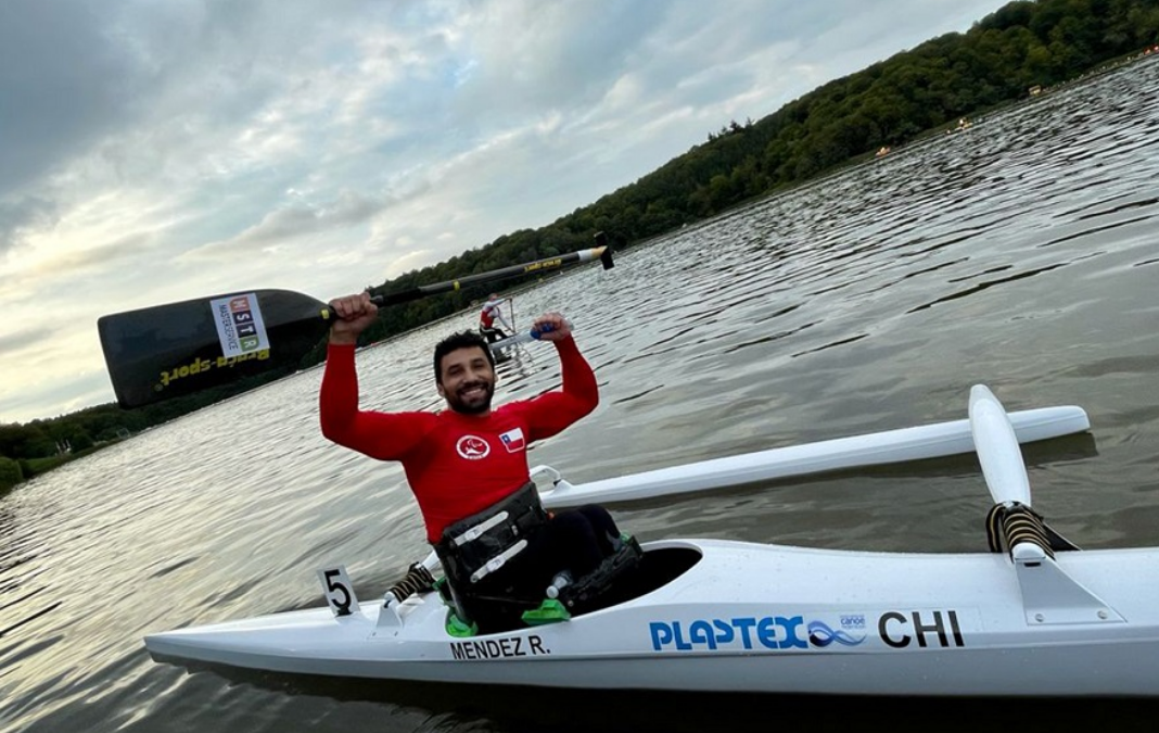 Fotografía de un hombre sobre un kayak levantando un remo con los brazos, en medio de un lago