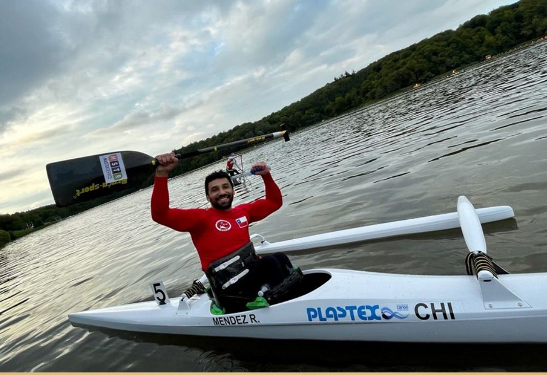Fotografía de un hombre sobre un kayak levantando un remo con los brazos, en medio de un lago