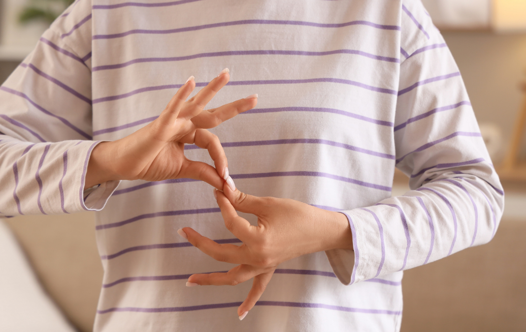 Persona con polera blanca con rayas, y haciendo seña de legua de señas con sus manos