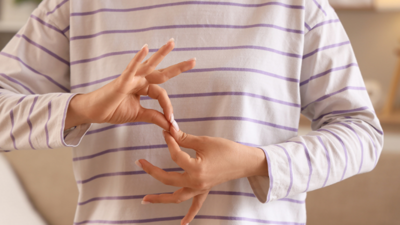 Persona con polera blanca con rayas, y haciendo seña de legua de señas con sus manos