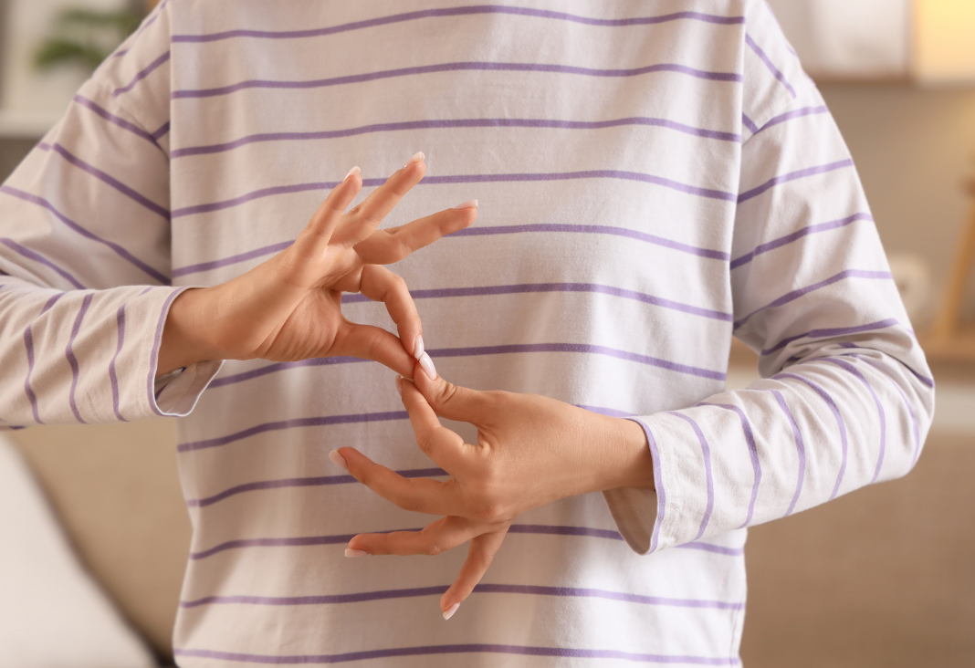 Persona con polera blanca con rayas, y haciendo seña de legua de señas con sus manos