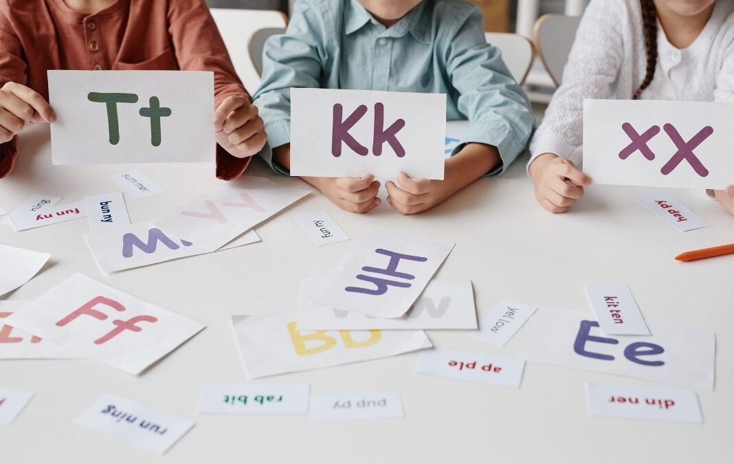 Tres niños mostrando hojas con las letras T K y X