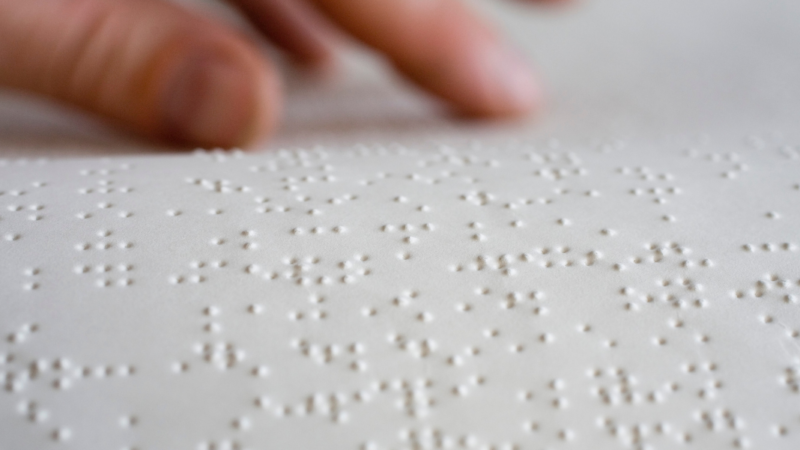 Una mano sobre una hoja escrita con Braille