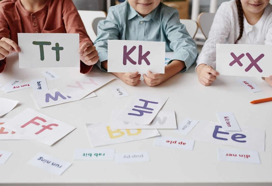 Tres niños mostrando hojas con las letras T K y X