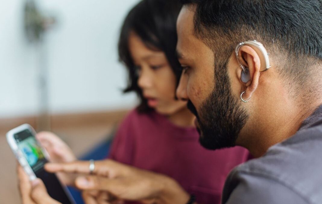 Hombre Sordo con audífono mirando un celular junto a un iño