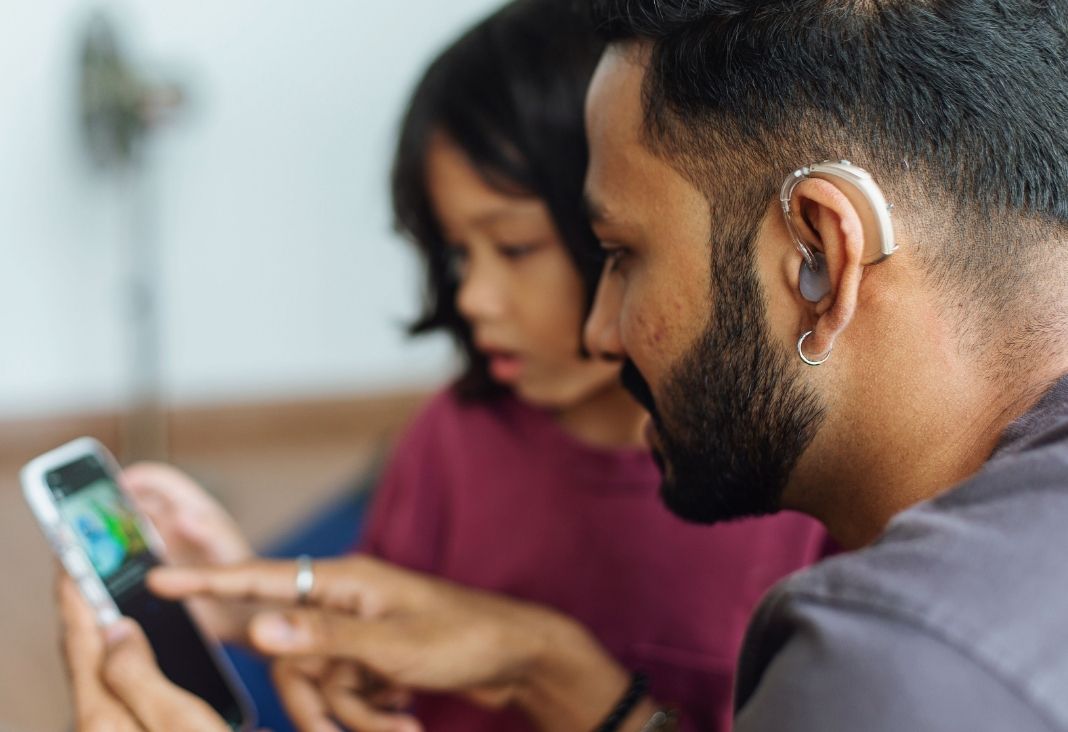 Hombre Sordo con audífono mirando un celular junto a un iño
