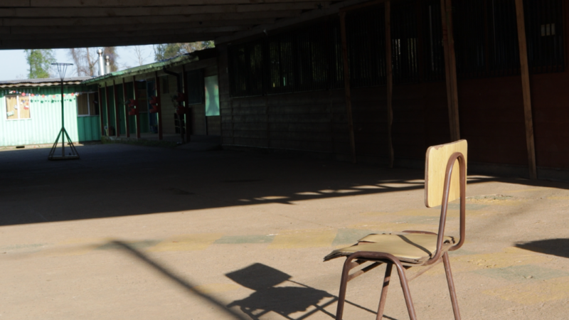 Fotografía de una silla de escuela y de fondo una escuela
