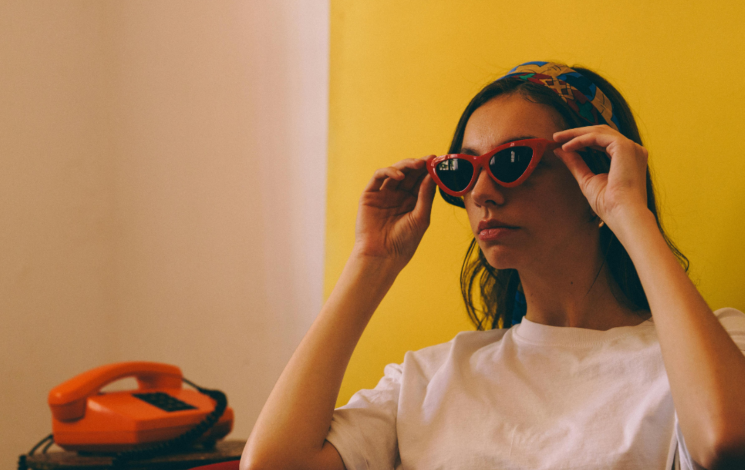 Mujer de persil sujetando gafas de sol retro y junto a ella un teléfono rojo retro