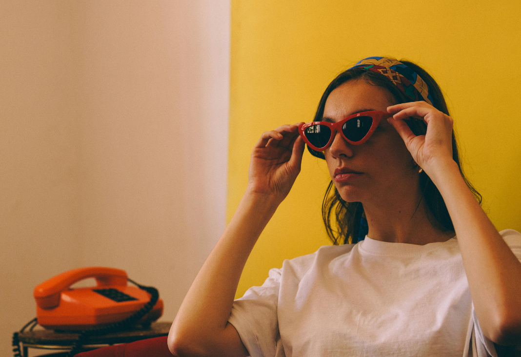 Mujer de persil sujetando gafas de sol retro y junto a ella un teléfono rojo retro