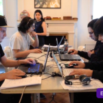 Cuatro jóvenes sentados frente a computadores en torno a una mesa