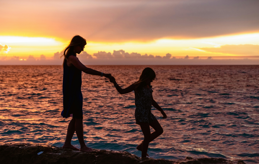 Fotografía de la silueta de una mujer y una niña de la mano en una playa al atardecer
