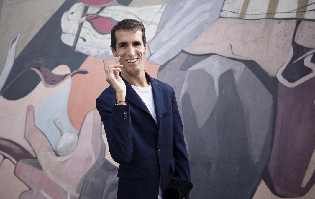 Hombre posando a una fotografía y de fondo un mural