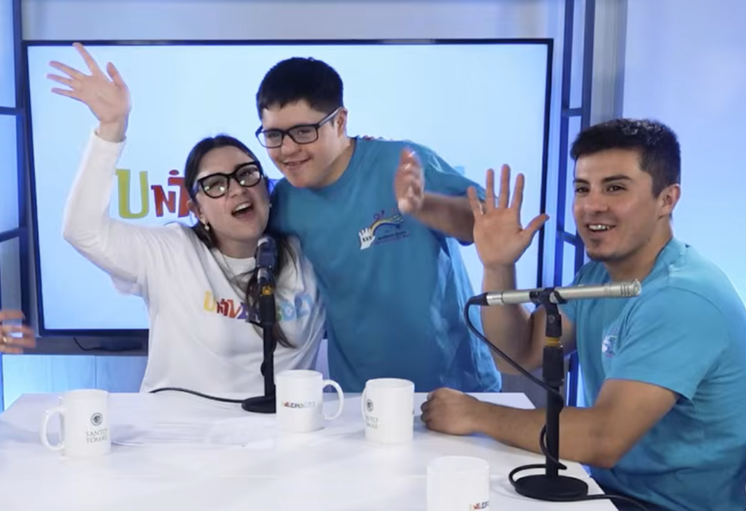 Una mujer abrazando a un joven con síndrome de Down y un hombre junto a ellos. Los tres saludando a la cámara en un estudio de televisión