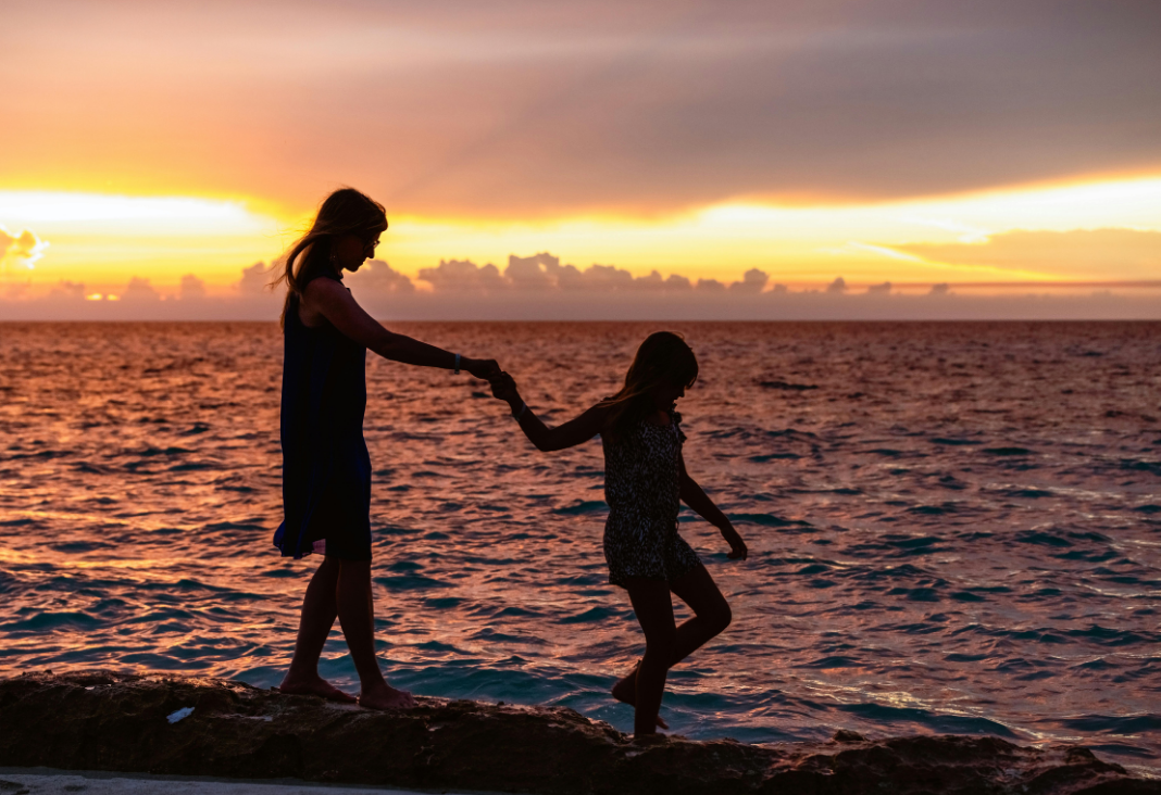 Fotografía de la silueta de una mujer y una niña de la mano en una playa al atardecer